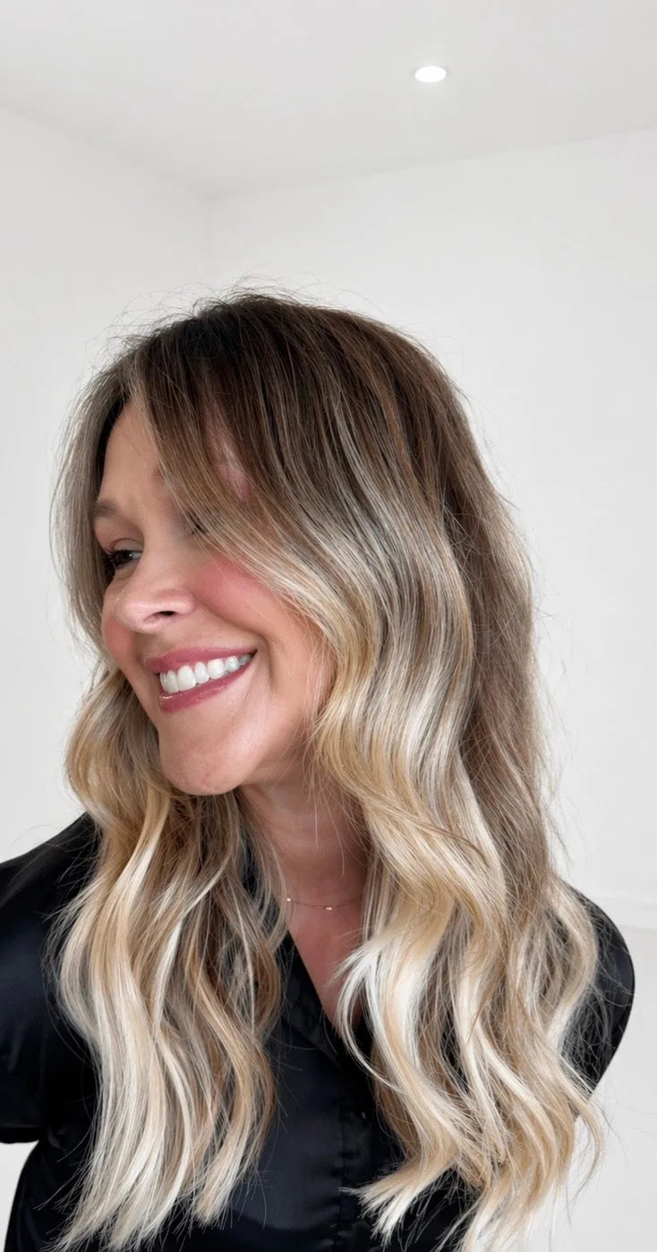 Side view of client with long wavy blonde balayage Mago Method extensions