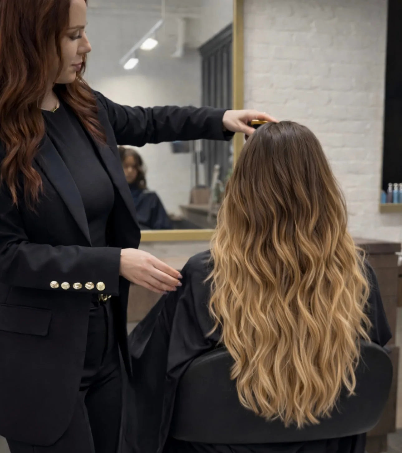 Stylist examining client's long wavy blonde balayage Mago Method extensions
